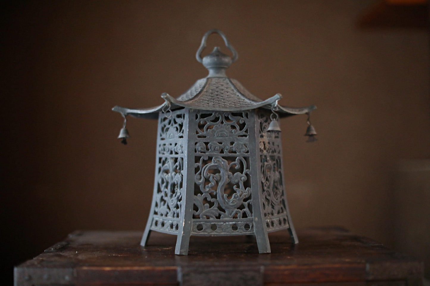 A decorative metal lantern with intricate designs and a pointed roof sits on a wooden surface.