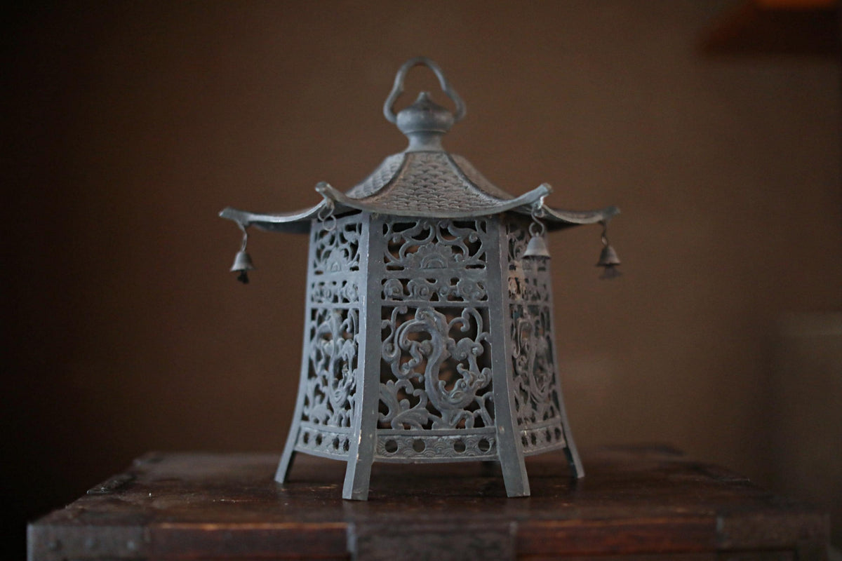 A decorative metal lantern with intricate designs and a pointed roof sits on a wooden surface.
