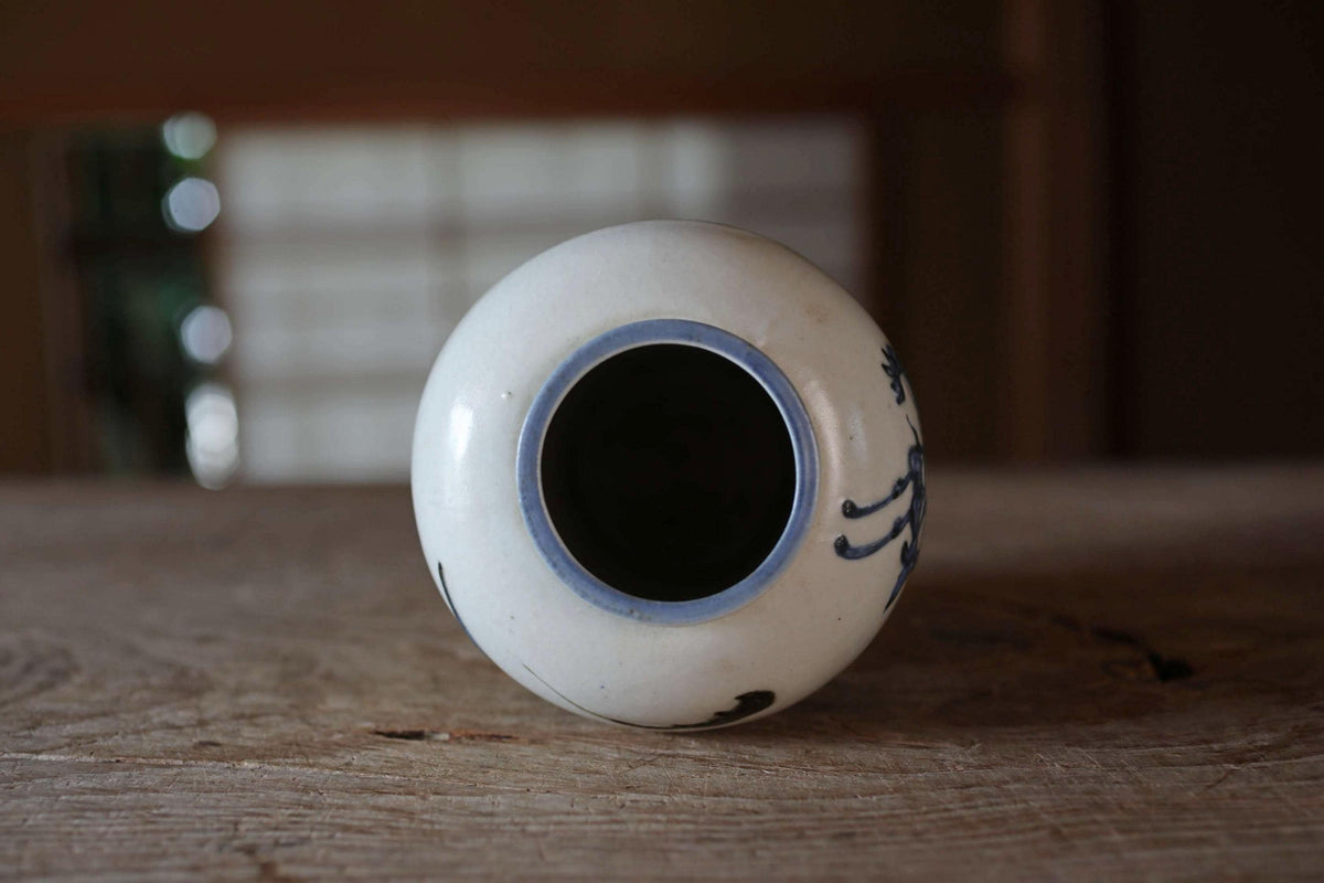 A white ceramic vase with a blue rim and a black design on it, sitting on a wooden surface.