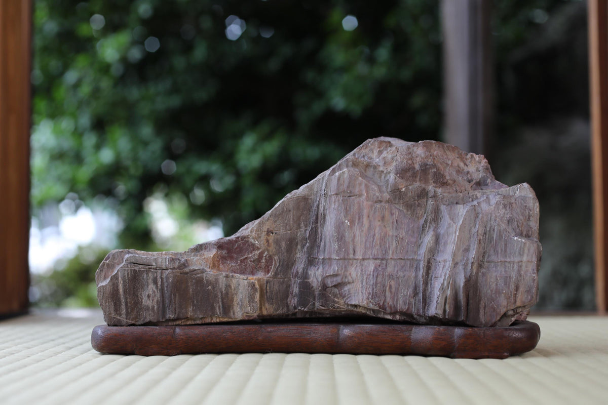 A large, irregularly shaped rock rests on a wooden base, positioned on a wooden surface.