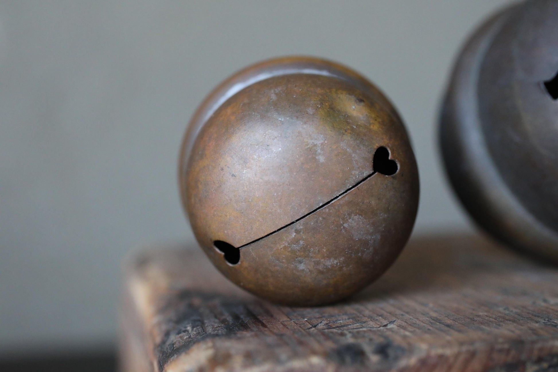 A close-up image of a rusted metal bell with a heart-shaped cutout, resting on a wooden surface.
