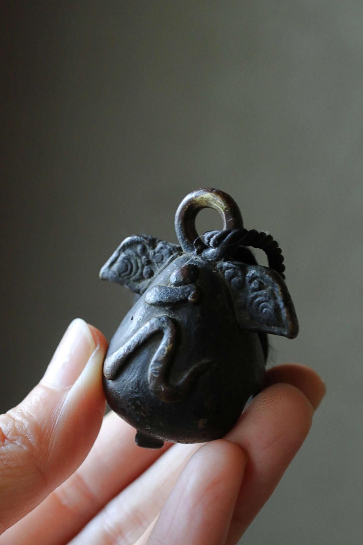 A person's hand holding a small, black, metal bell with an intricate design on it.