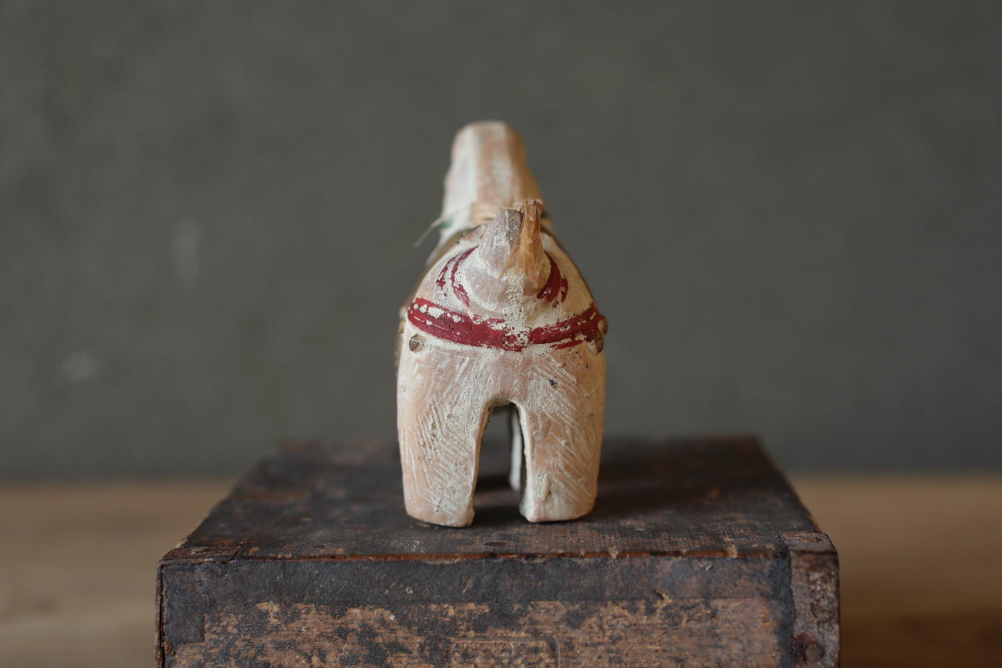 A wooden toy horse with a red ribbon around its neck is sitting on a wooden box against a gray background.