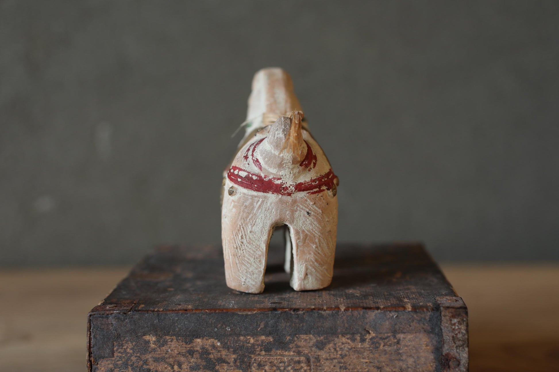 A wooden toy horse with a red ribbon around its neck is sitting on a wooden box against a gray background.