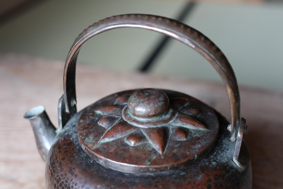 A close-up image of a metal teapot with a decorative lid, featuring a star-shaped design.
