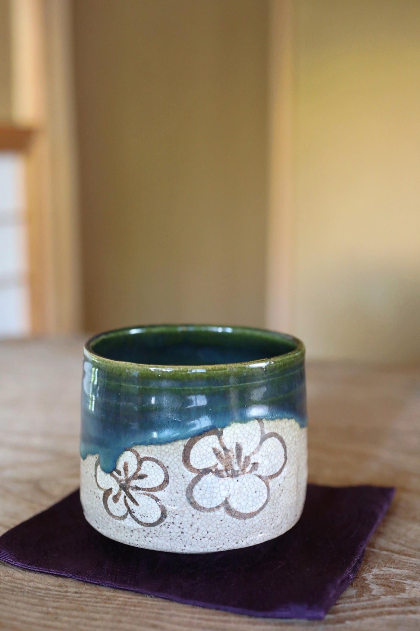 A ceramic mug with a floral design sits on a purple napkin on a wooden table.