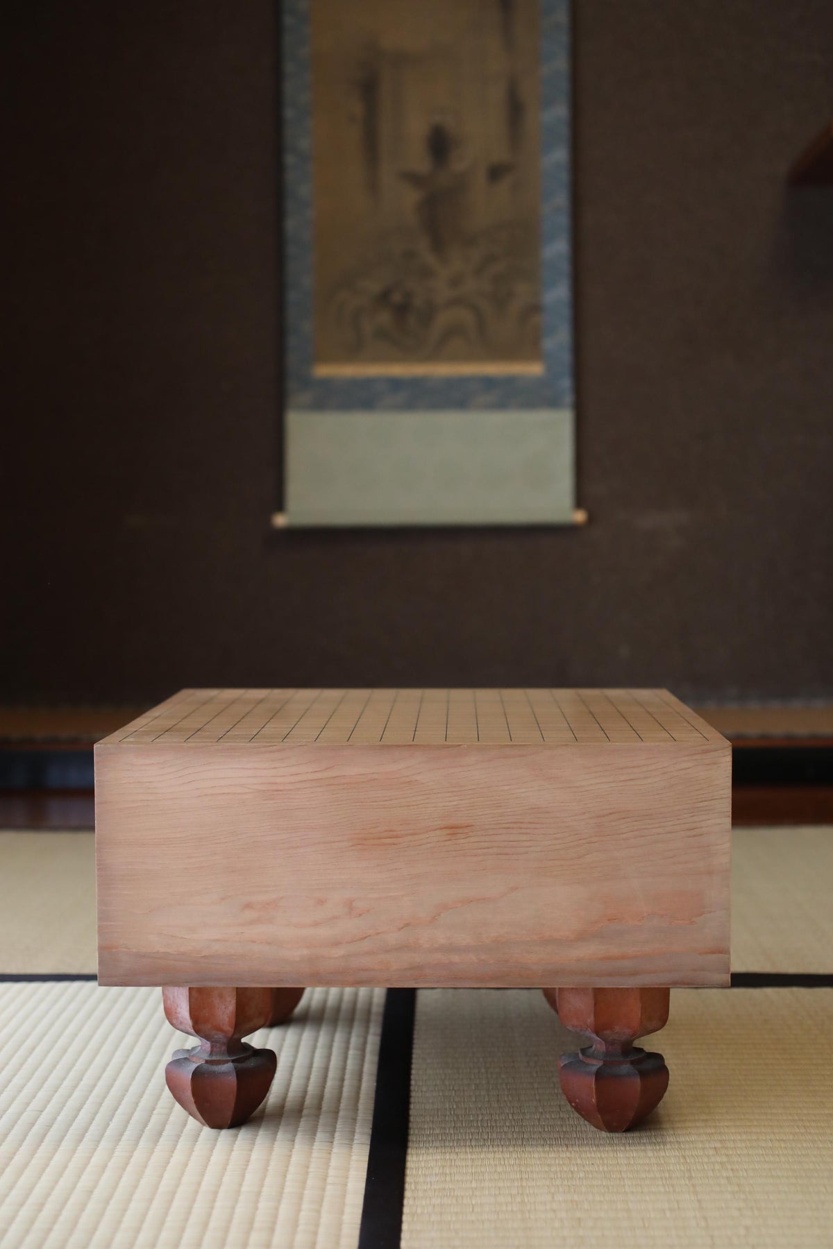 a wooden table with a checkerboard pattern on its surface, placed on a tatami mat. In the background, there is a framed artwork hanging on the wall.