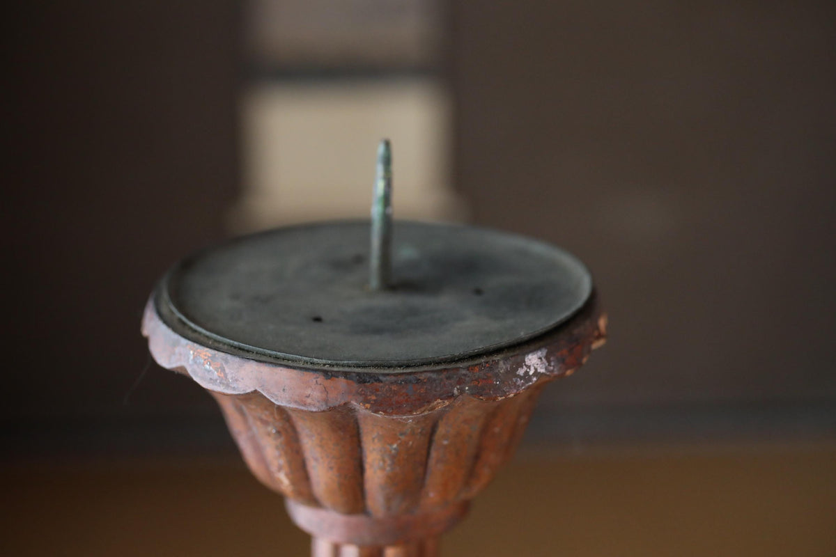 An old, rusted metal candelabra with a green metal piece sticking out of the top.