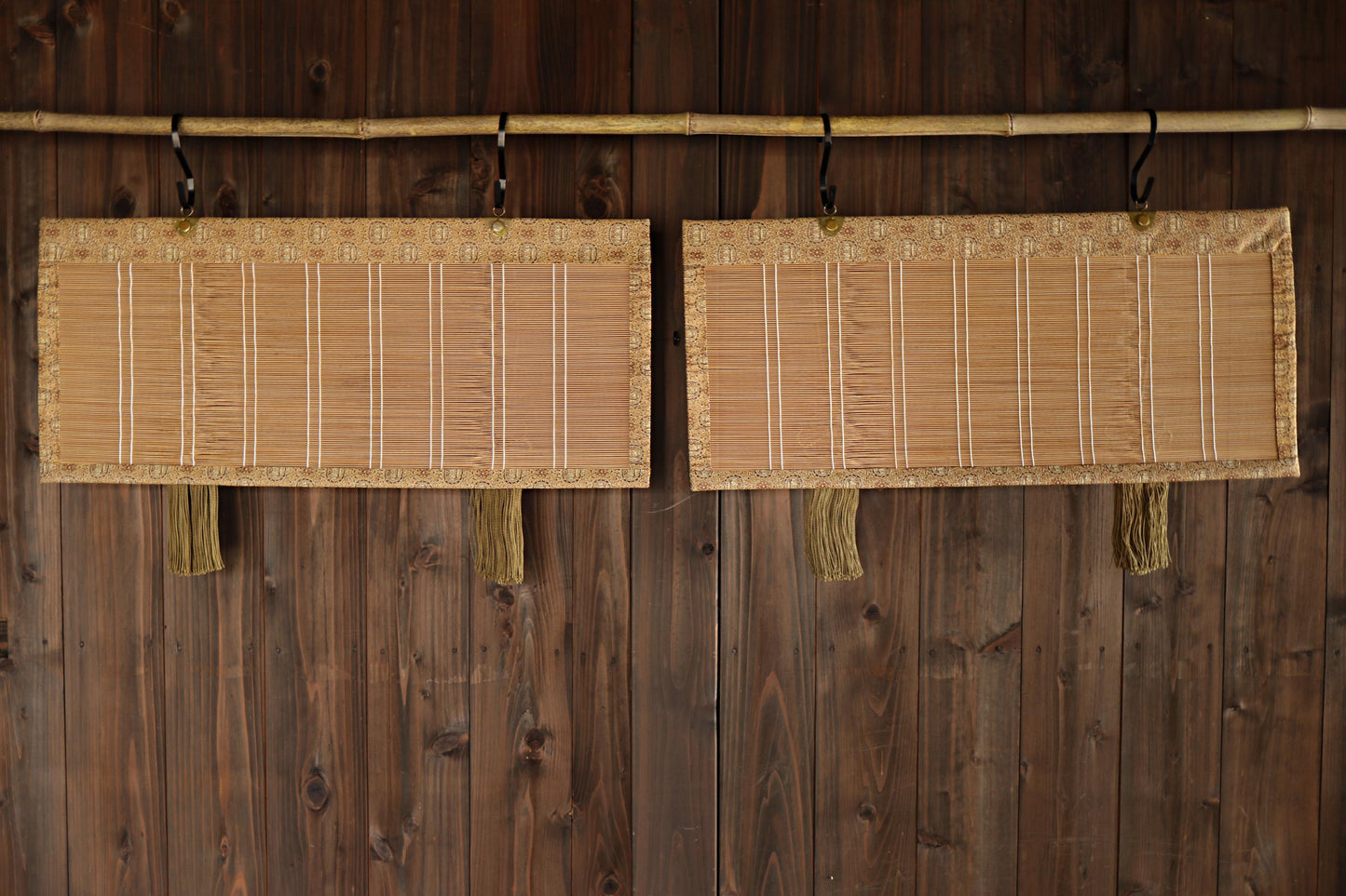 Two bamboo wall hangings with a woven design are hanging on a wooden wall.