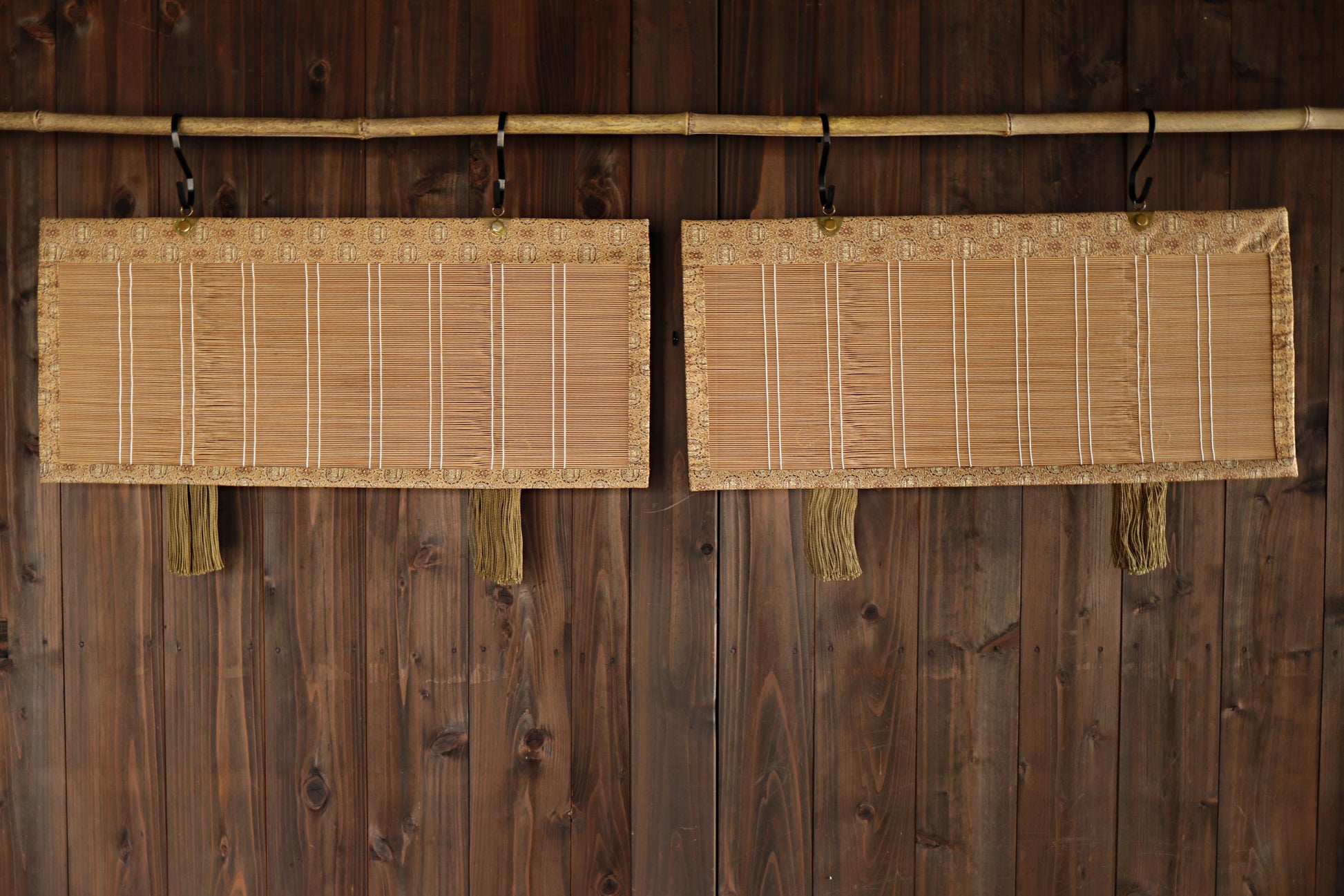 Two bamboo wall hangings with a woven design are hanging on a wooden wall.