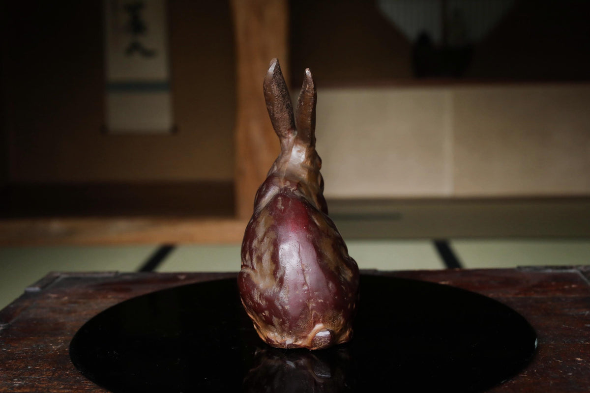 A ceramic rabbit figurine sits on a black circular surface, with a blurred background suggesting an indoor setting.