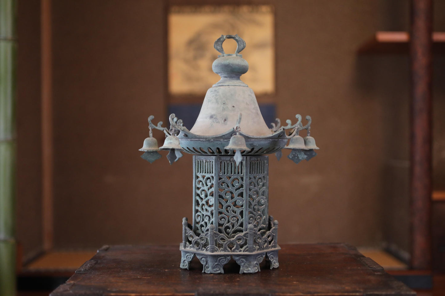 A decorative metal lantern with intricate designs and a bell-like structure, placed on a wooden surface.