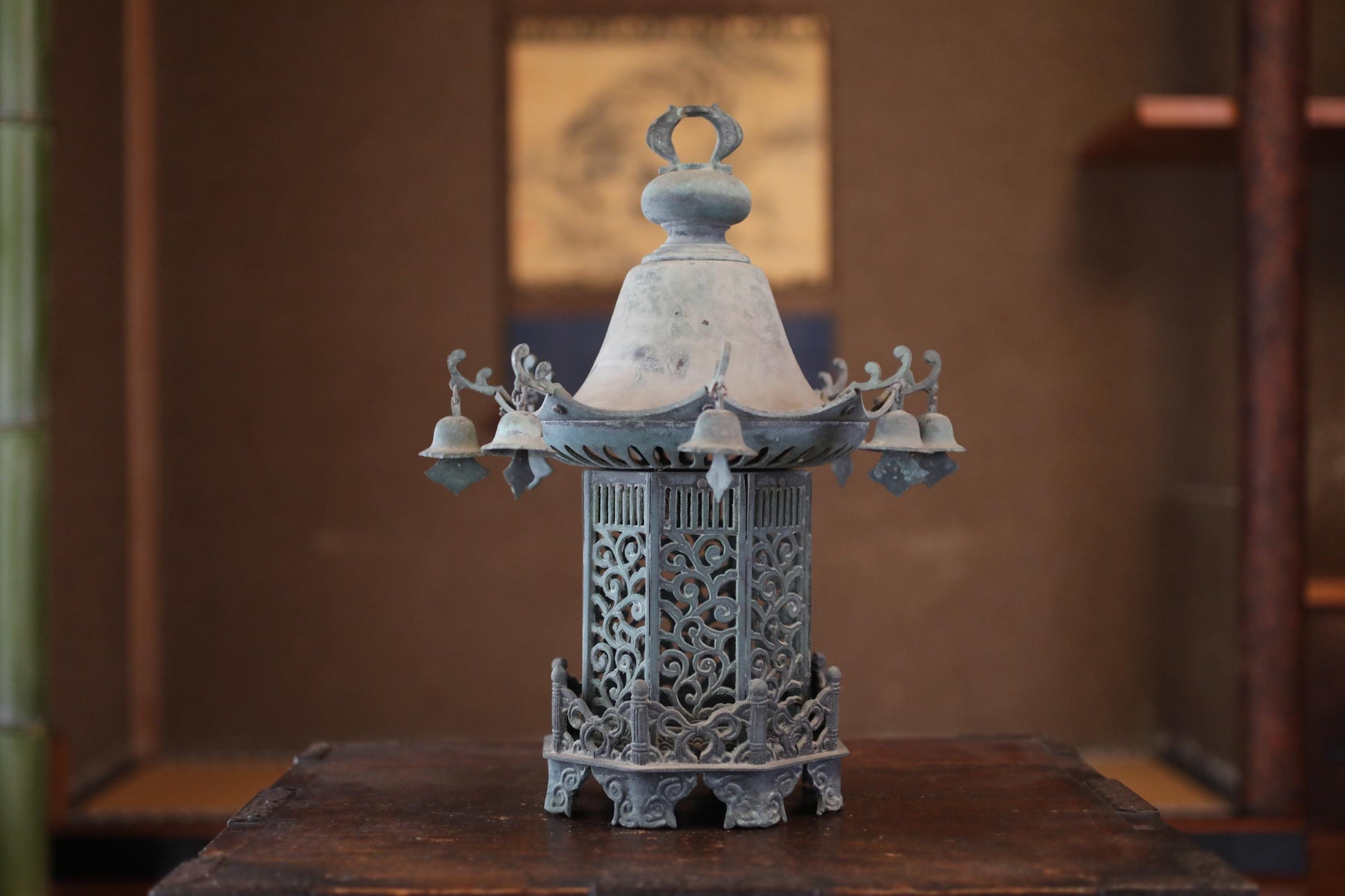 A decorative metal lantern with intricate designs and a bell-like structure, placed on a wooden surface.