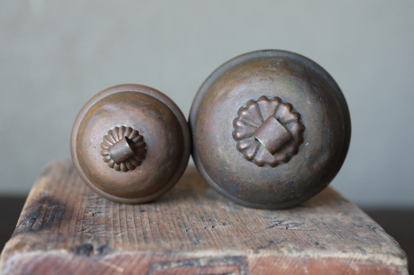 Two antique brass knobs with ornate designs sit on a wooden surface.
