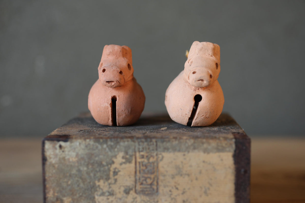 Two clay figurines of animals, possibly pigs, sitting on a metal surface.