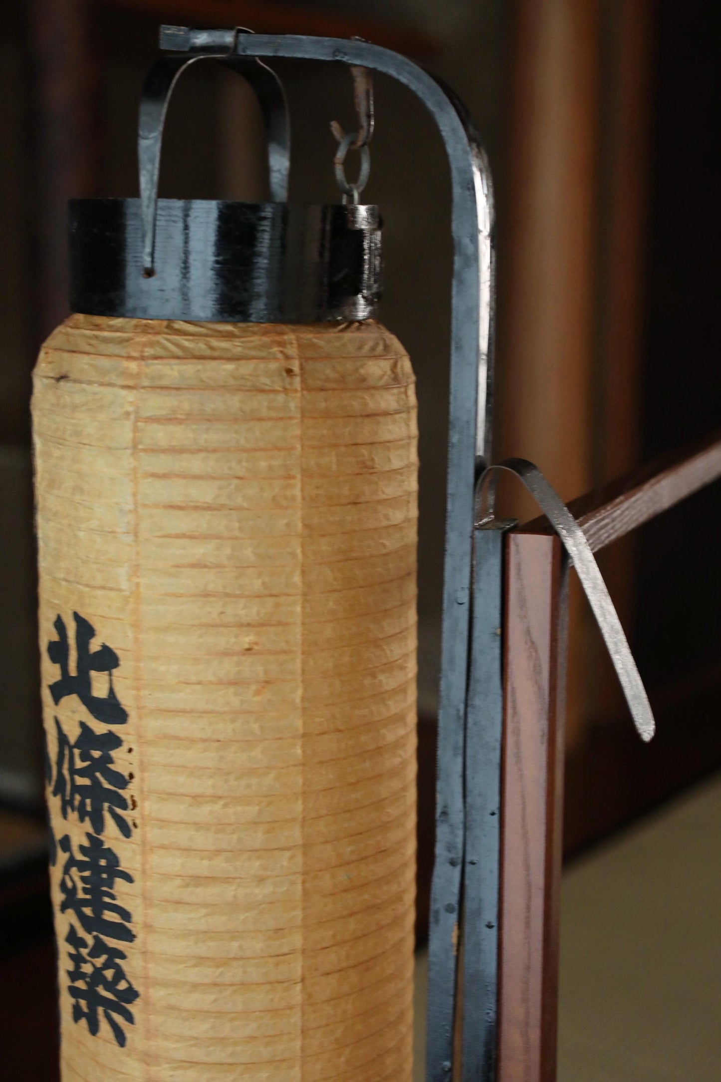 A close-up view of a traditional Japanese lantern, featuring a wooden frame and a black metal hook.