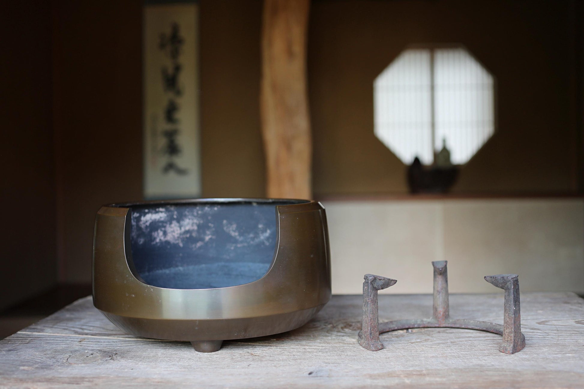 a traditional Japanese tea set, including a bowl and a metal stand, placed on a wooden table. The background features a window with a traditional Japanese design.