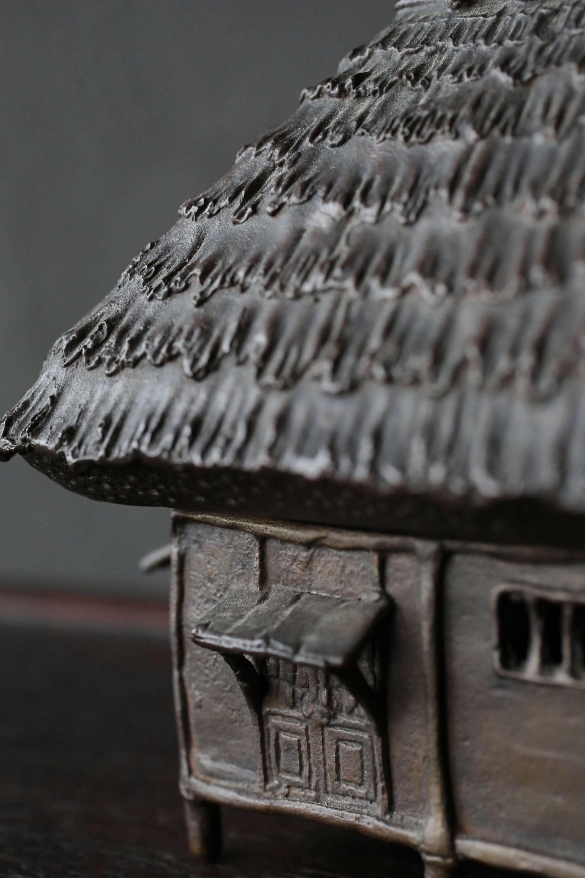 A close-up view of a metal sculpture depicting a small, intricately designed house with a thatched roof.