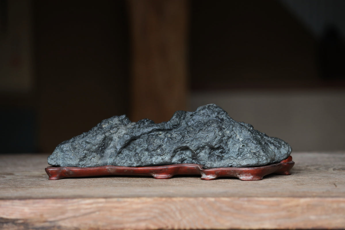 A large, dark gray rock sits on a wooden surface, resting on a red stand.