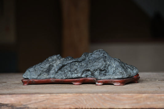 A large, dark gray rock sits on a wooden surface, resting on a red stand.