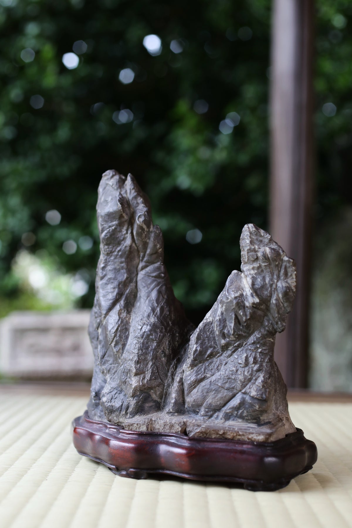 A stone sculpture of two large rocks sits on a wooden base, with a blurred natural background.