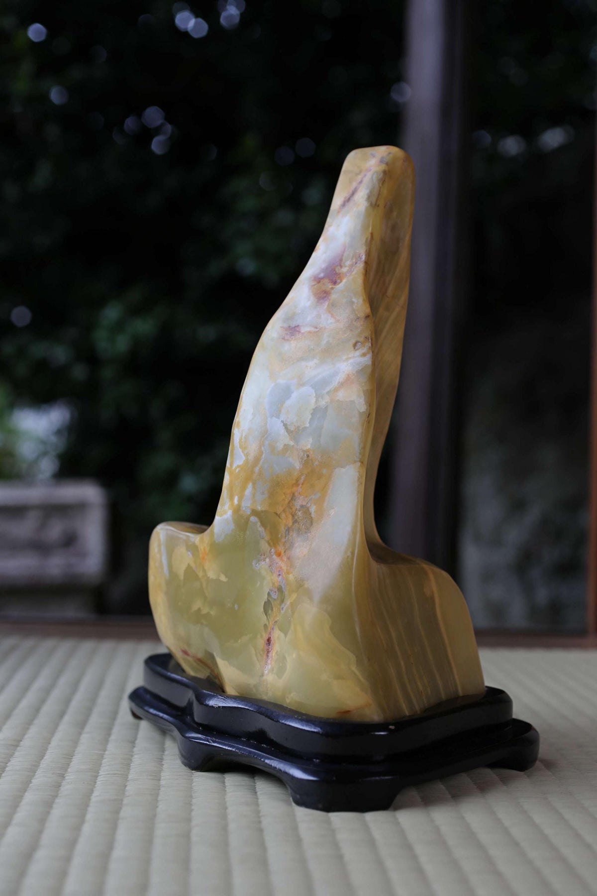 a large, yellowish-brown stone sculpture with a unique, curved shape, sitting on a black stand.