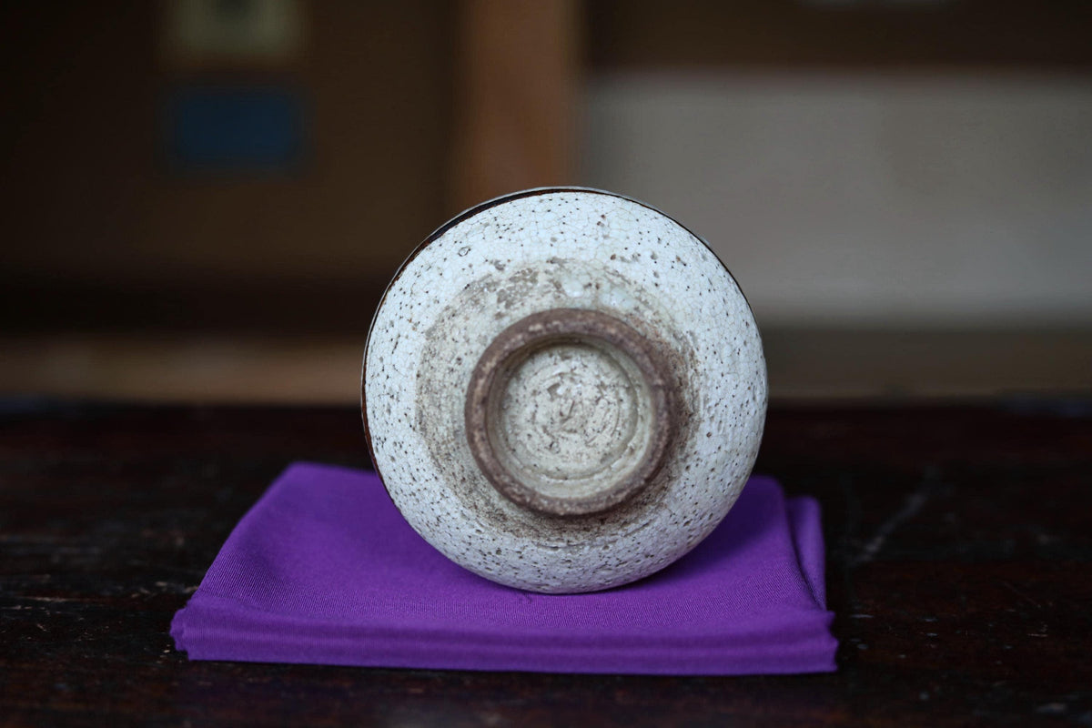 A white ceramic bowl with a brown rim sits on a purple cloth on a wooden surface.