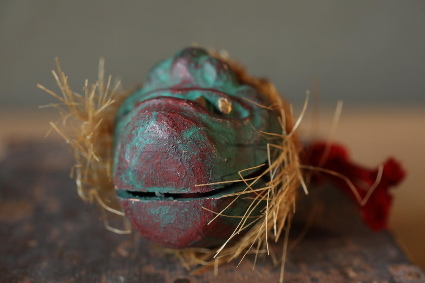 A close-up image of a weathered, green metal object with a red and blue color scheme, partially covered in straw.