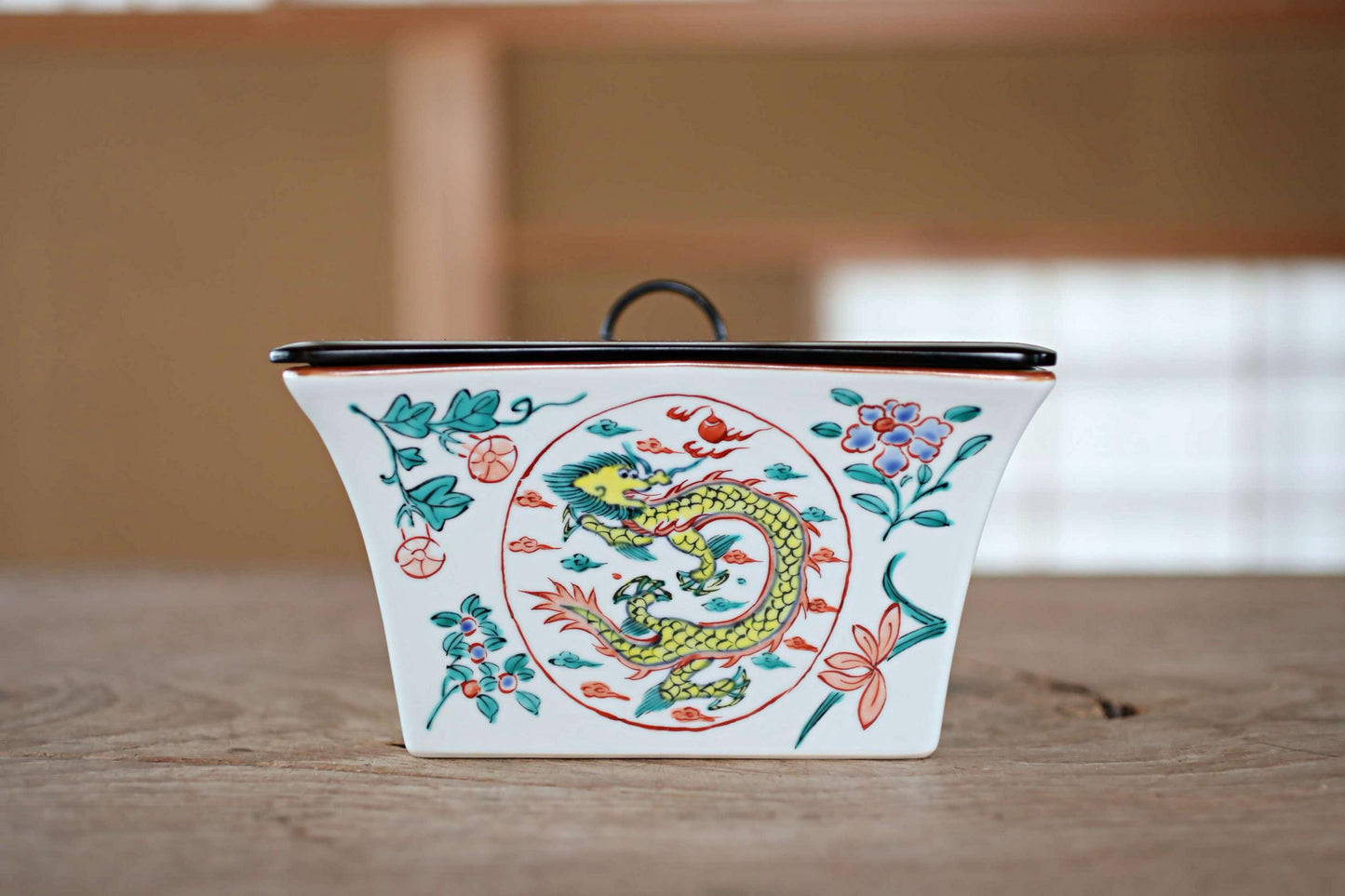 A ceramic container with a dragon design on it, placed on a wooden surface.