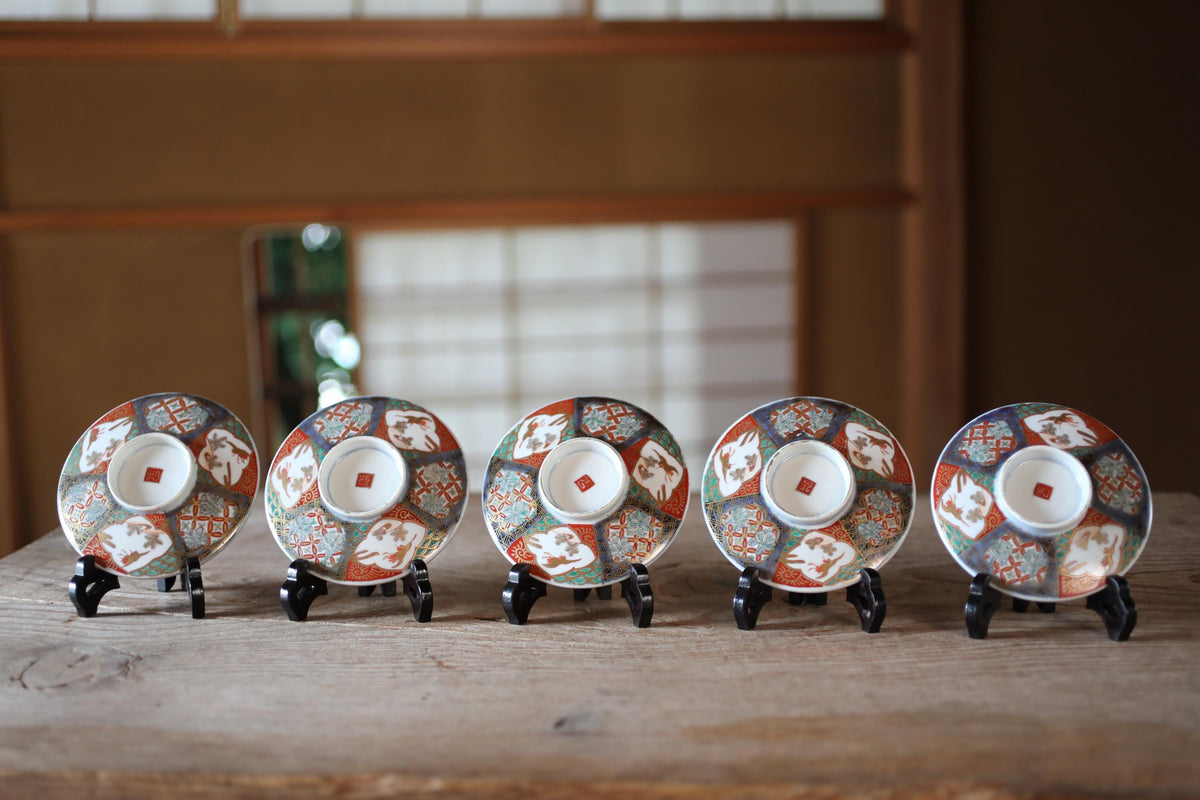 A row of five colorful ceramic plates or cups with intricate designs, displayed on a wooden surface.