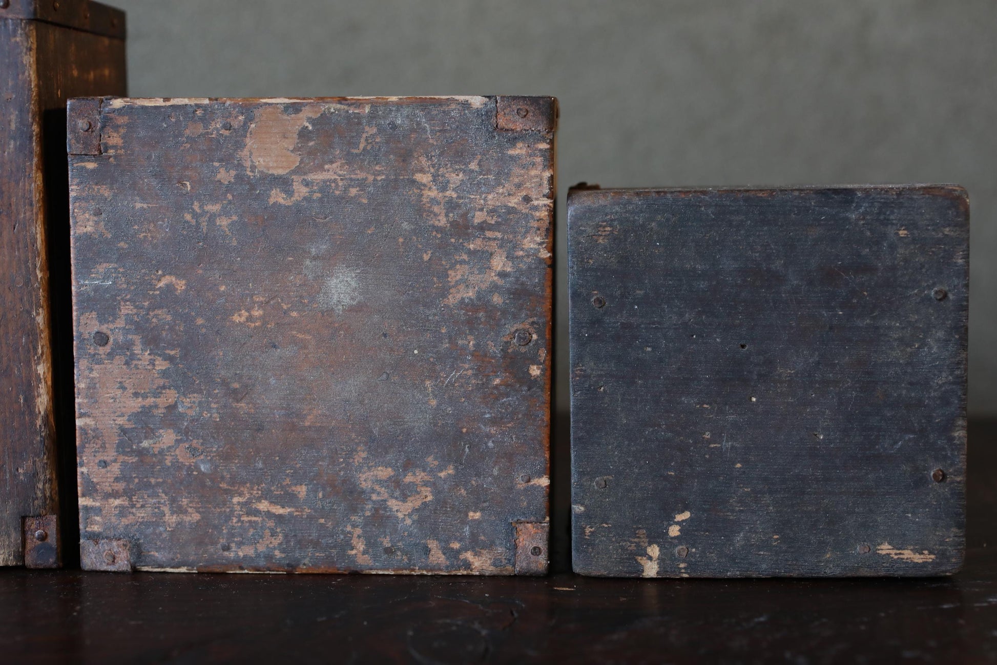 two old, weathered wooden boxes with peeling paint and visible signs of wear, sitting on a dark surface.
