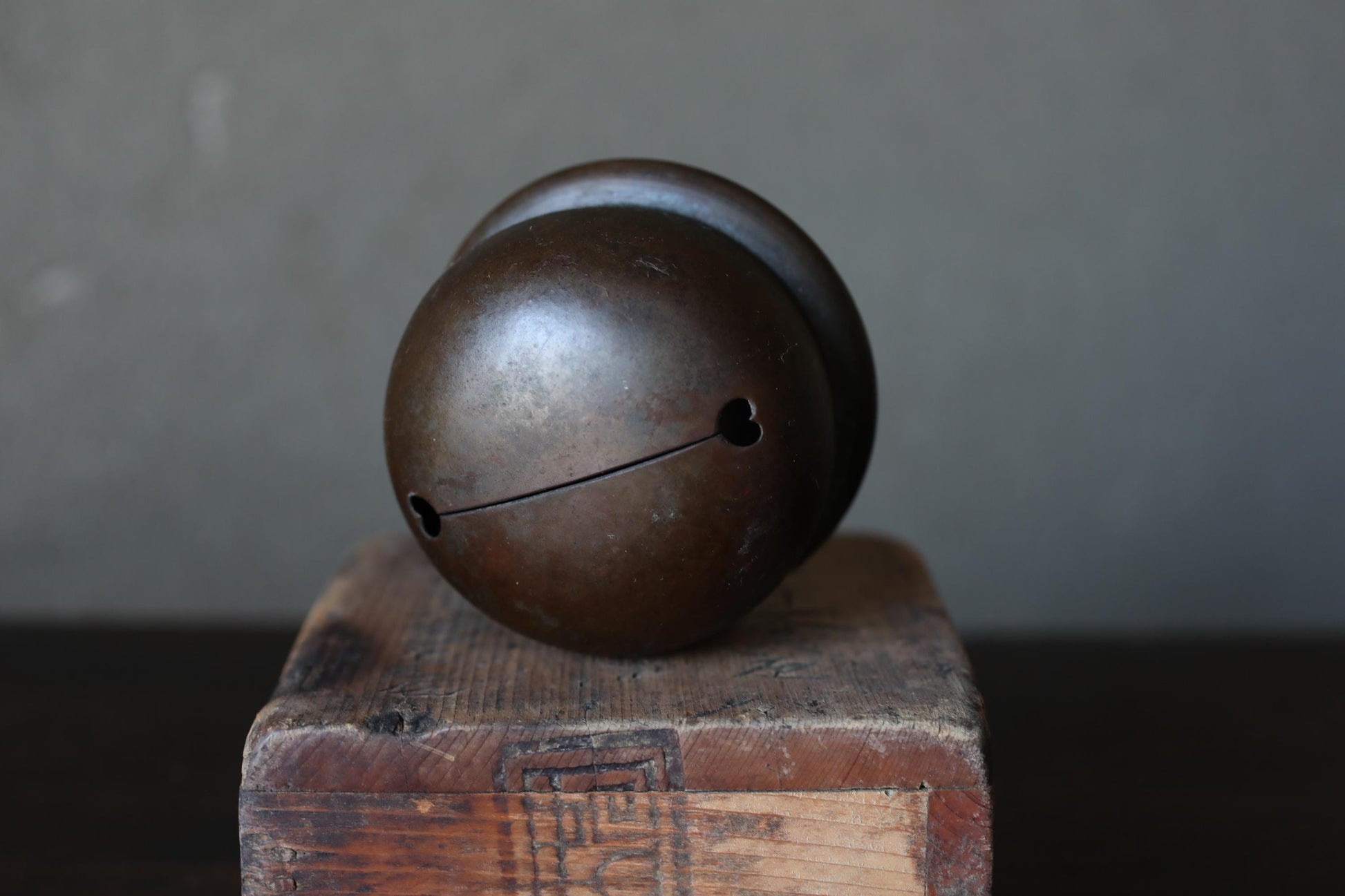 A round, dark-colored bell or ornament is placed on a wooden surface, with a blurred background.