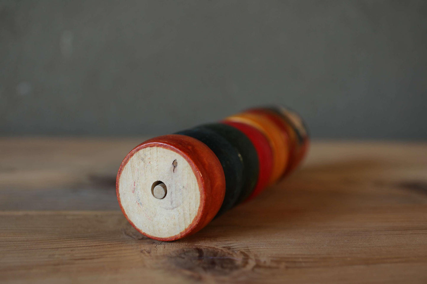 A wooden toy with a red and black striped base rests on a wooden surface.