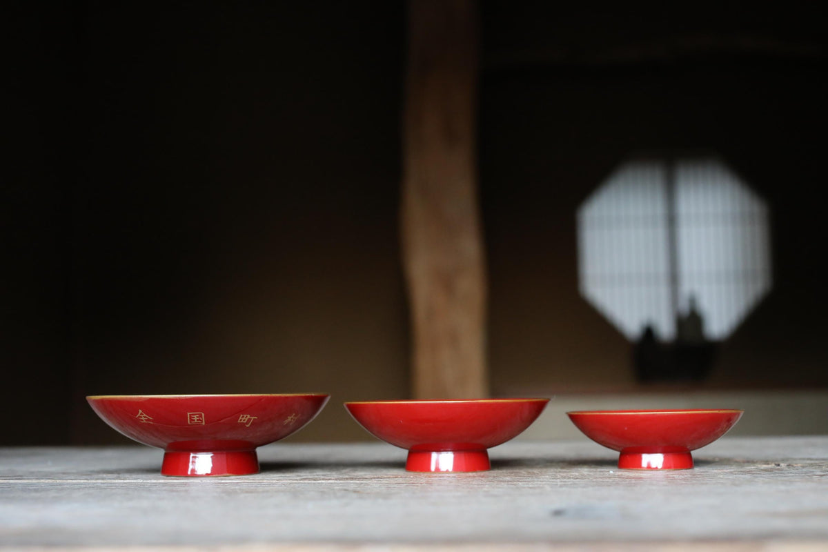 Three red bowls are arranged on a wooden surface, with a wooden beam and a window in the background.