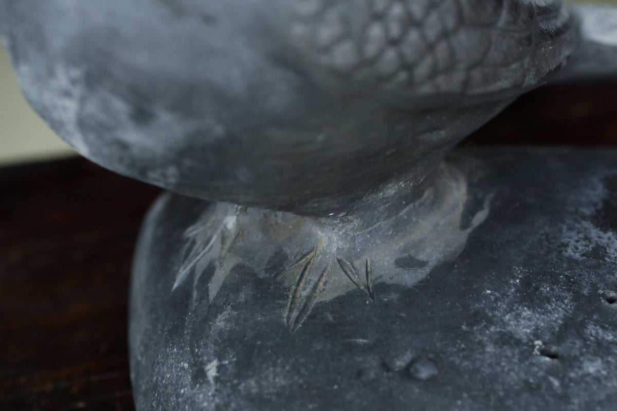 A close-up view of a stone or metal sculpture depicting a bird's foot, with intricate details and textures visible.