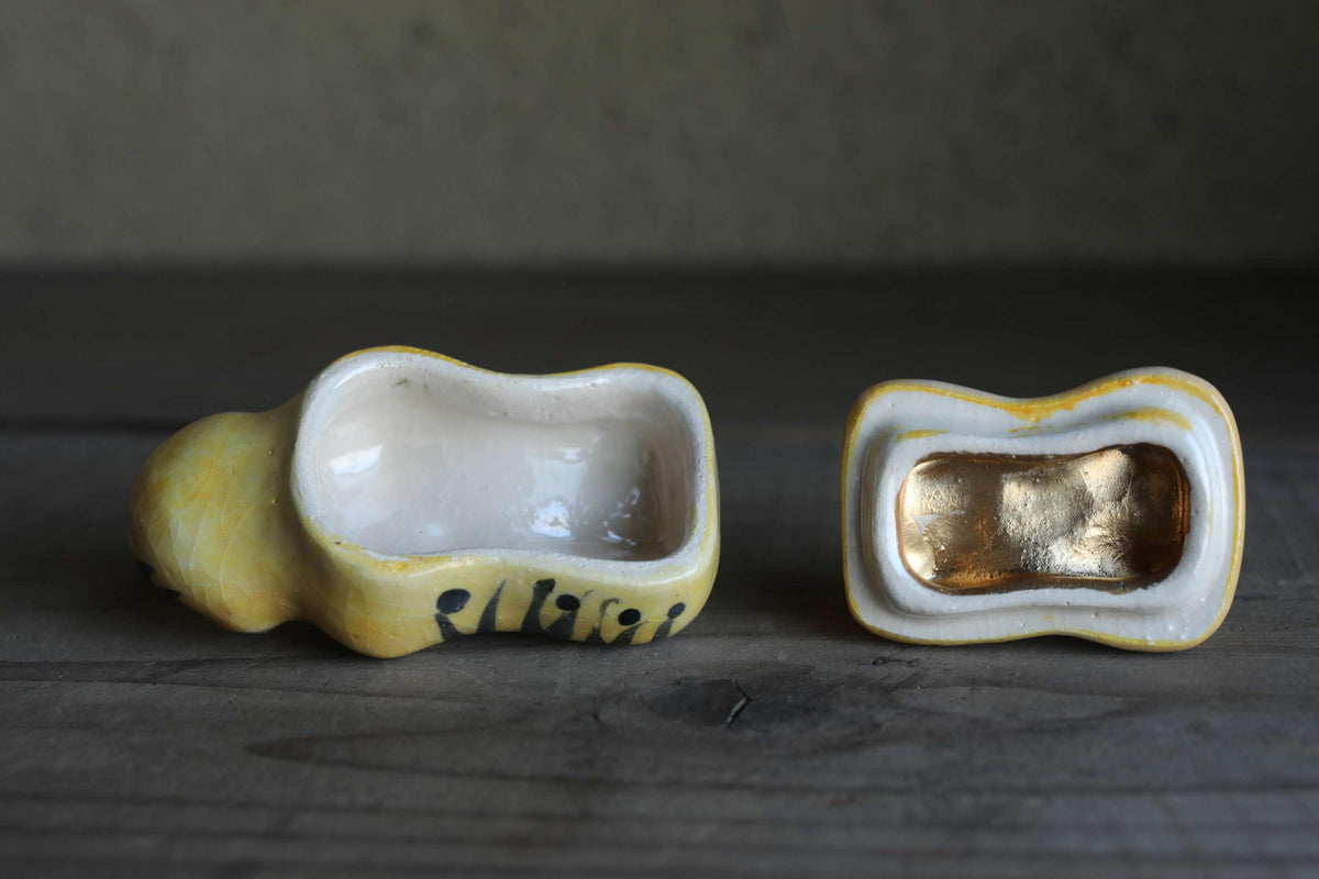Two ceramic objects, one with a gold interior and the other with a yellow exterior, are placed on a wooden surface.