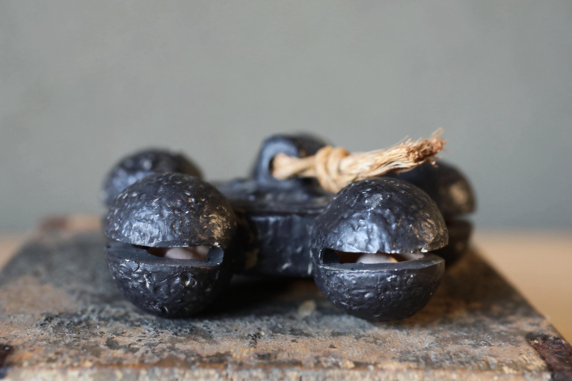 A close-up image of a set of black metal bells with a rope tied around them, resting on a wooden surface.