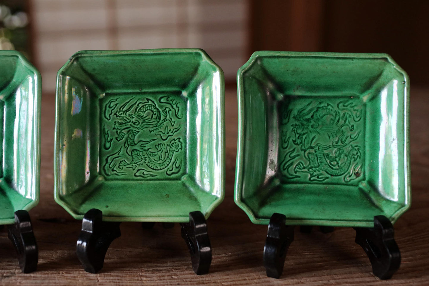 A row of green square plates with dragon designs on them, displayed on black stands.