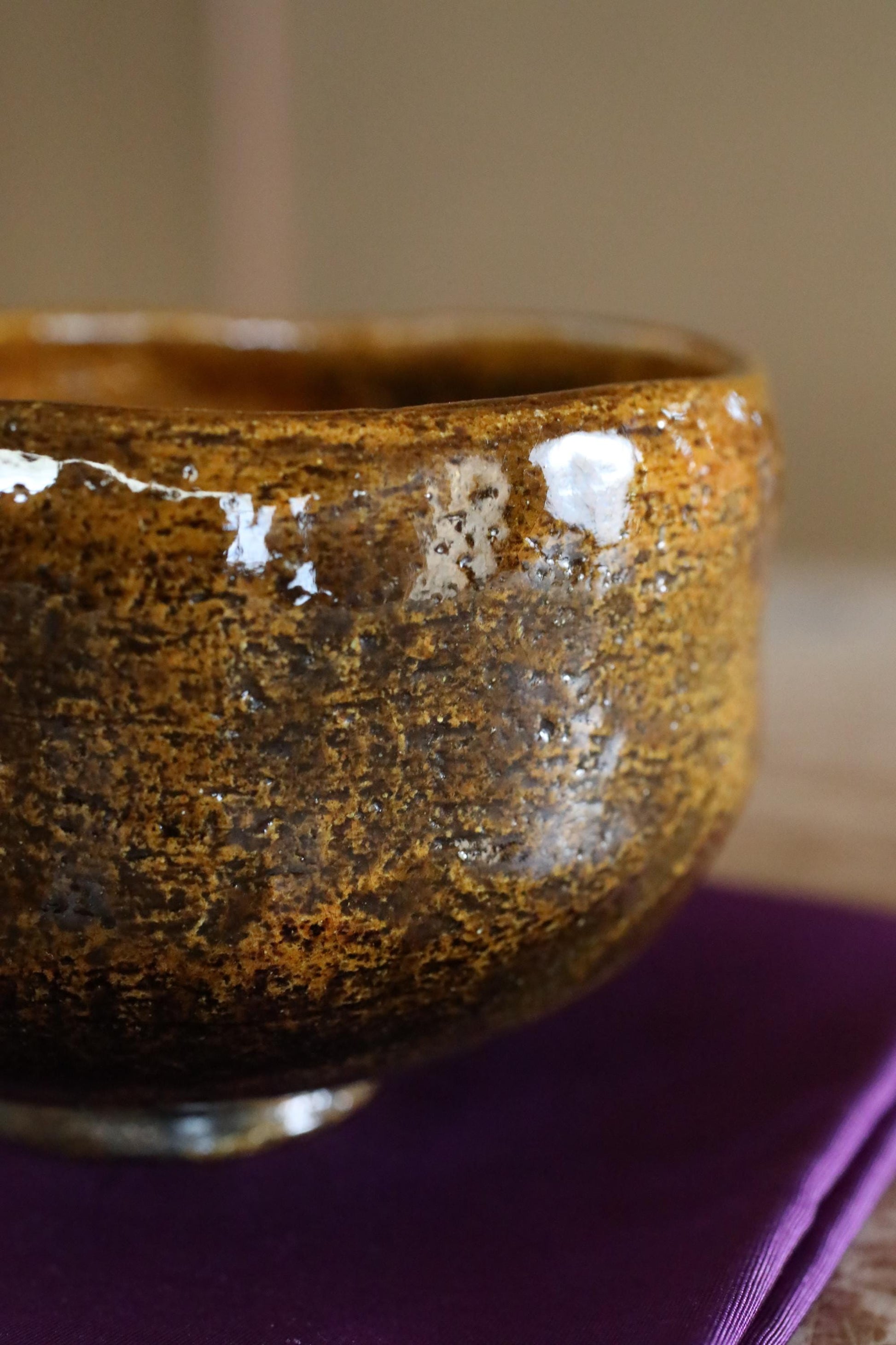 A close-up view of a textured, brown ceramic bowl with a purple background.