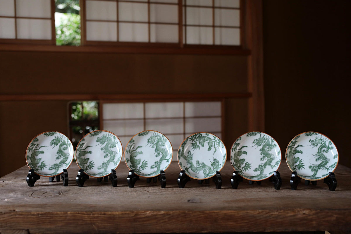 A row of six ornate plates with a dragon design, displayed on a wooden surface.