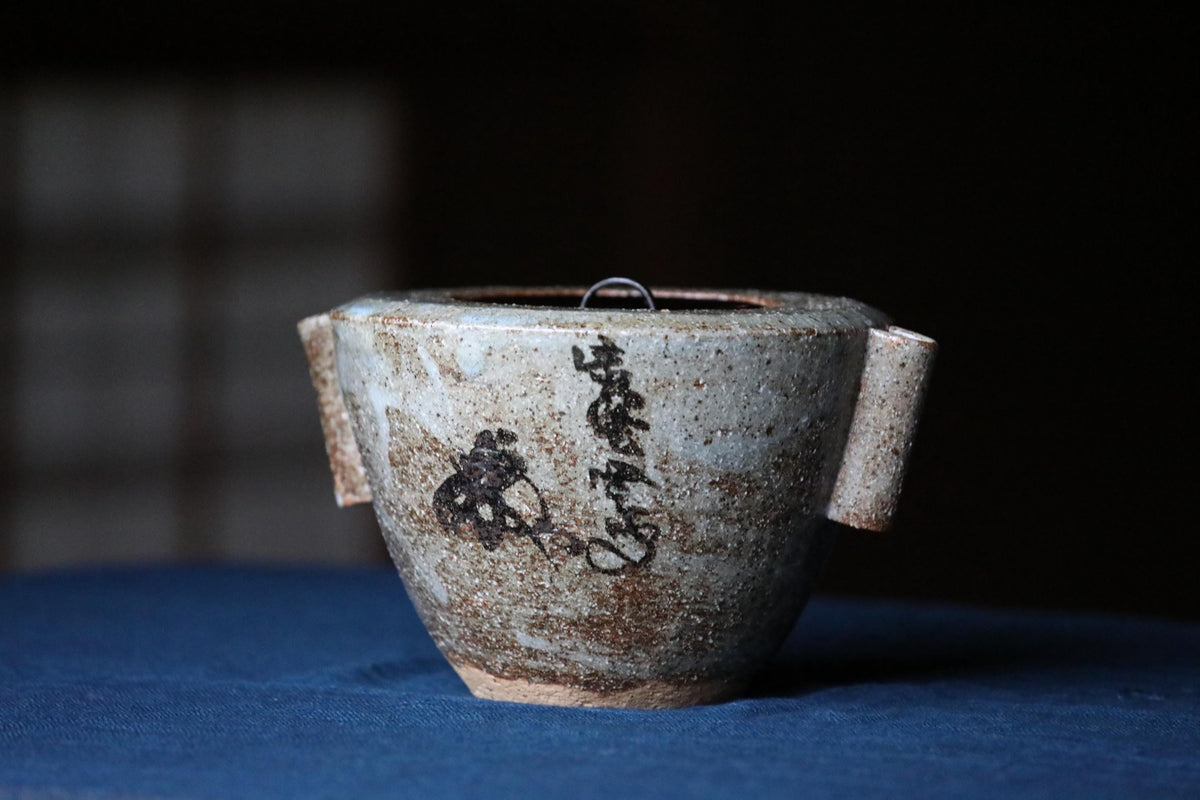 A ceramic teapot with a black design on its surface, sitting on a blue surface.
