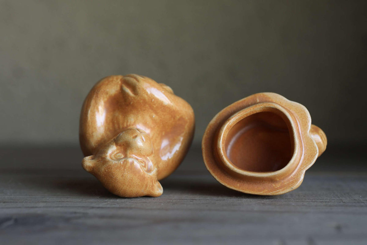 Two ceramic figurines of a monkey sitting on a wooden surface.