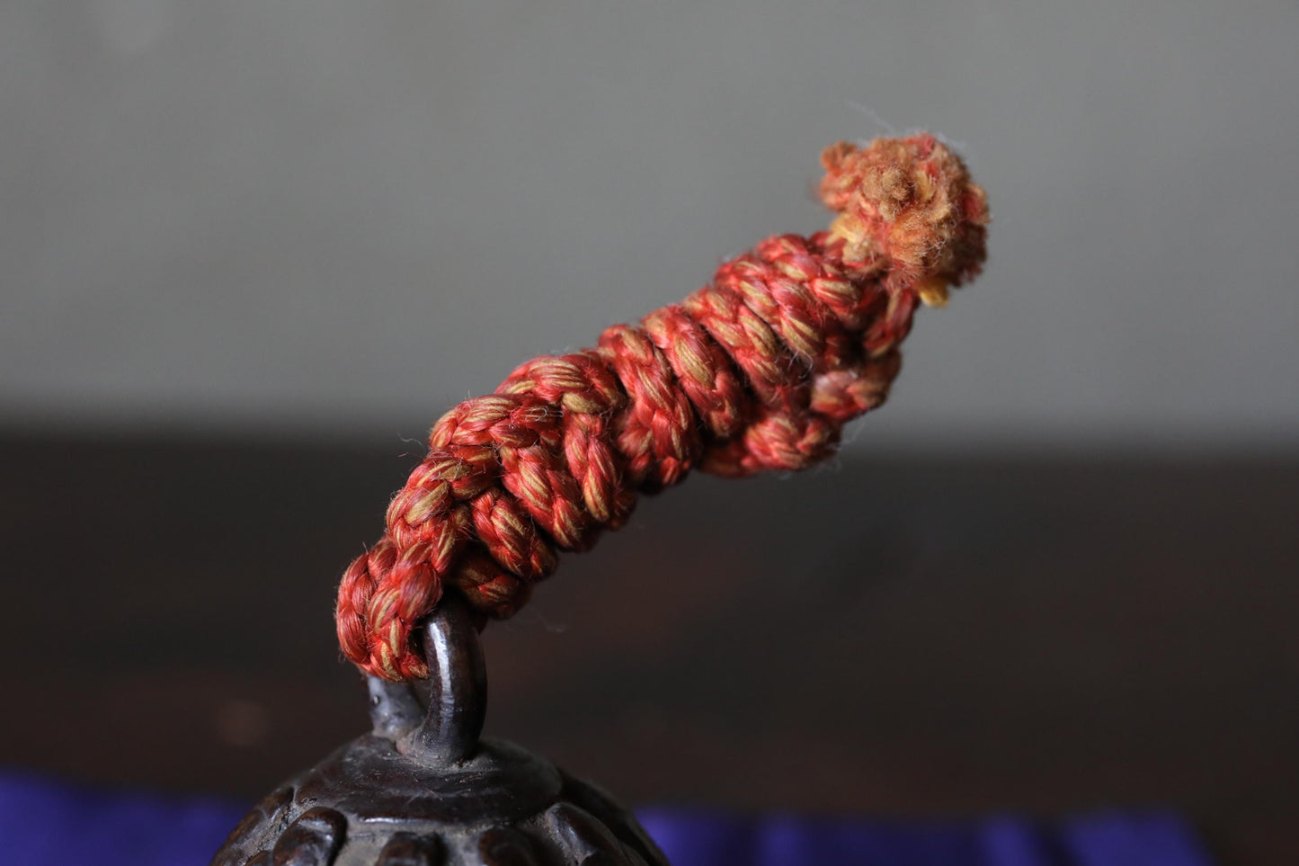 A close-up view of a red, braided rope or cord attached to a dark, textured surface.