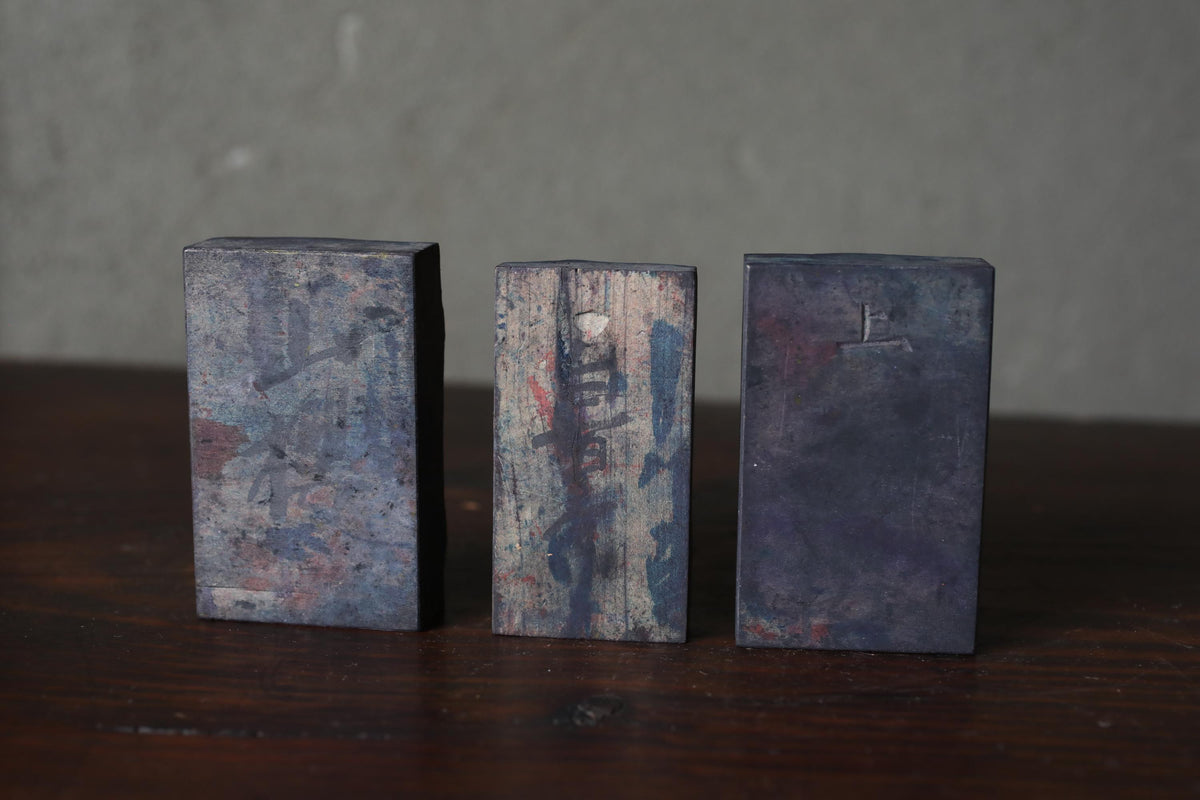 Three metal blocks with varying textures and colors are arranged on a wooden surface.