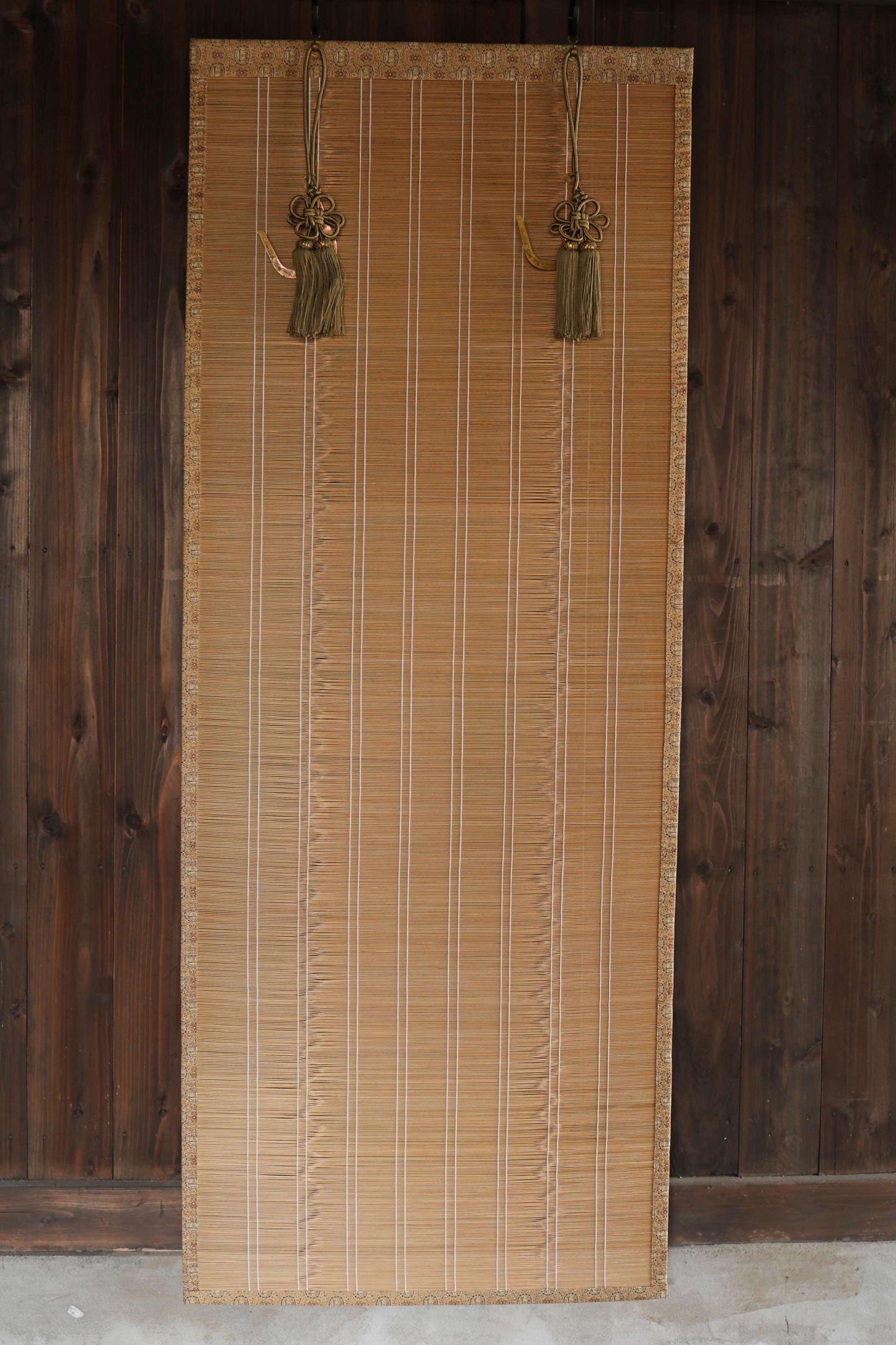 a bamboo blind with tassels hanging from the top, set against a wooden wall.
