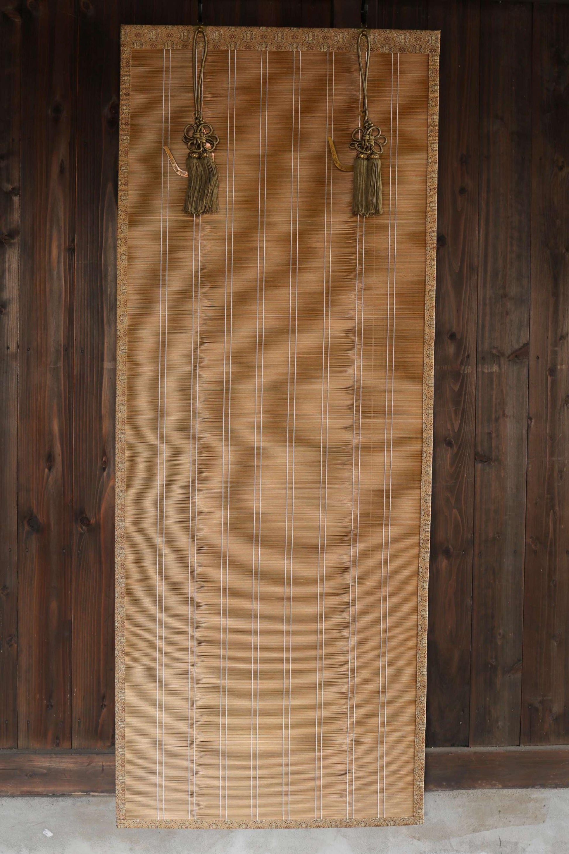 a bamboo blind with tassels hanging from the top, set against a wooden wall.