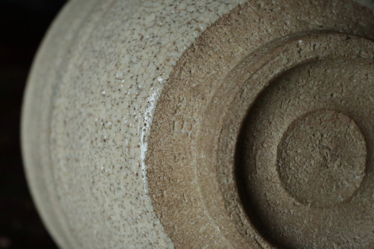 A close-up image of a ceramic bowl or vase with a textured surface, featuring a small marking or number on it.