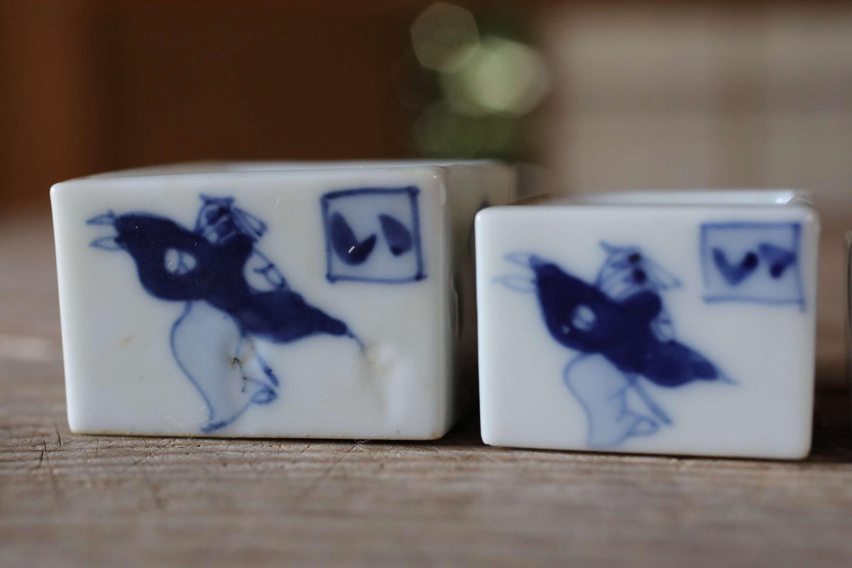 two square ceramic objects with blue designs, placed on a wooden surface.