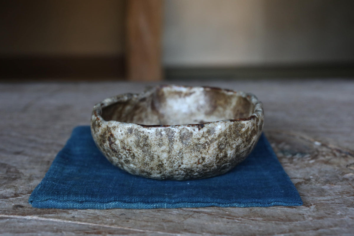 A ceramic bowl with a textured surface sits on a blue cloth on a wooden surface.