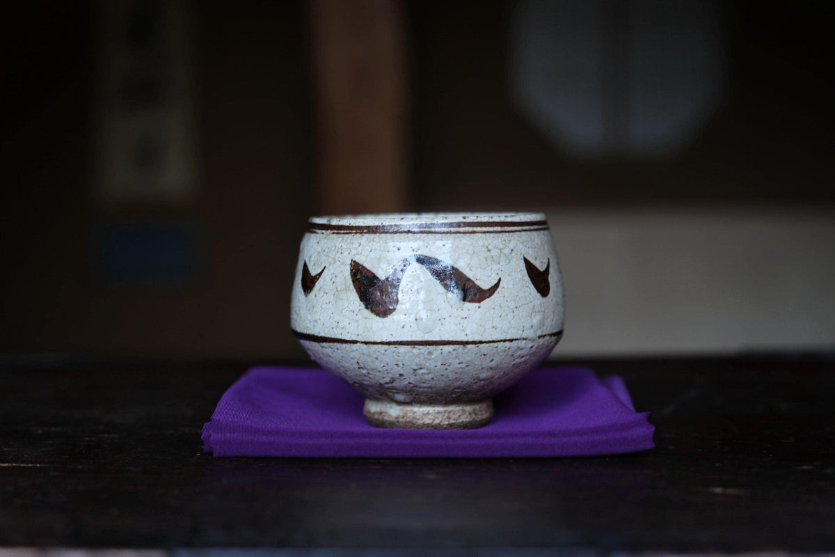 A white ceramic bowl with brown designs sits on a purple cloth on a wooden surface.